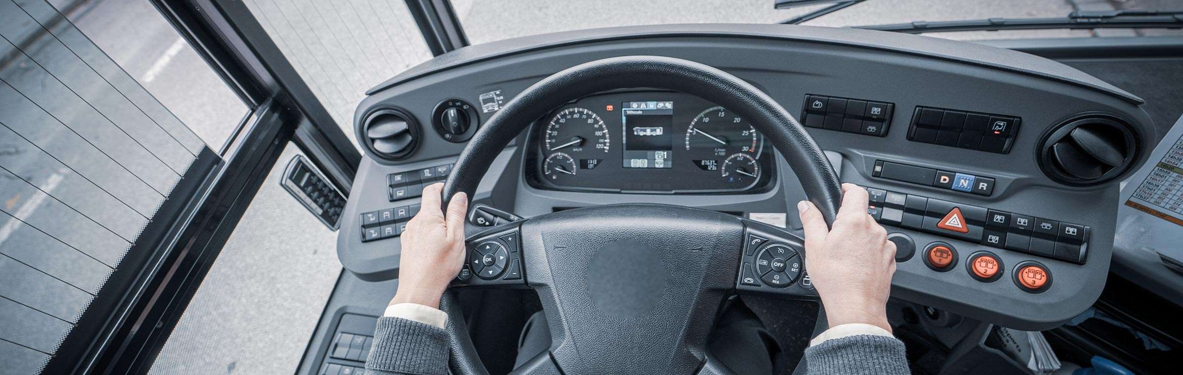 Closeup of a person's hands at a bus steering wheel.